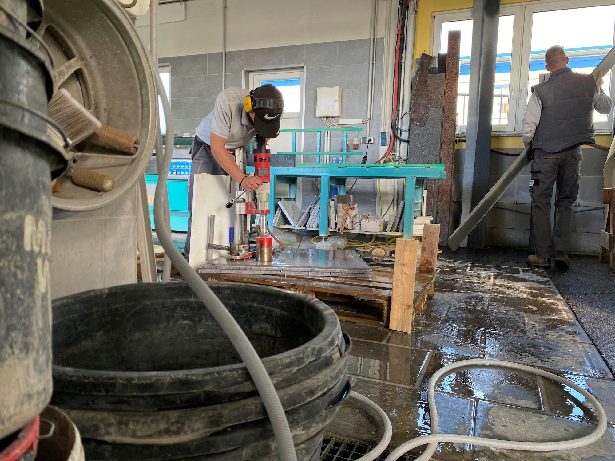 In einer Werkstatt bearbeitet der Azubi Pascal Elschenbroich eine polierte Natursteinplatte mit einem großen Bohrer.