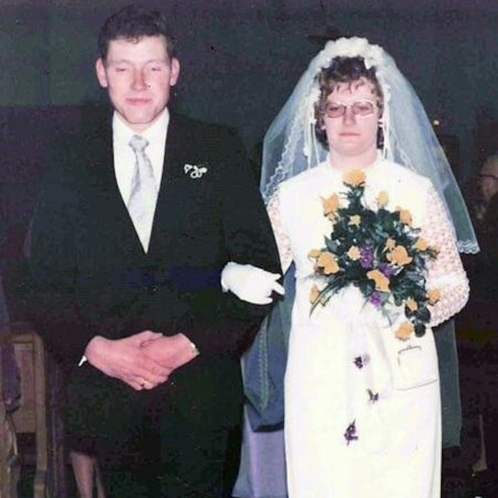Das Bild zeigt das Ehepaar Breuer bei seiner Hochzeit: Maria Breuer trägt ein Brautkleid und hält einen gelb-violetten Blumenstrauß in den Händen. Franz-Josef Breuer in einem schwarzen Anzug.