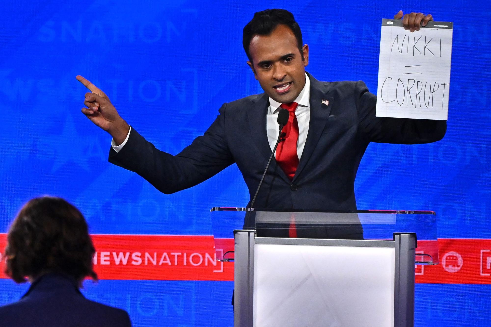 Vivek Ramaswamy hält ein Papier hoch. Darauf steht: „Nikki = korrupt“.