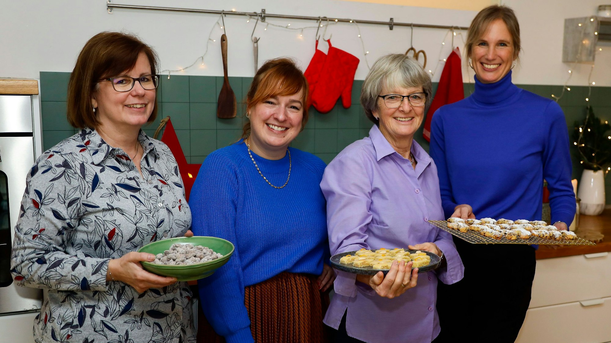 Vier Frauen stehen mit Plätzchen auf Tellern in einer Küche.