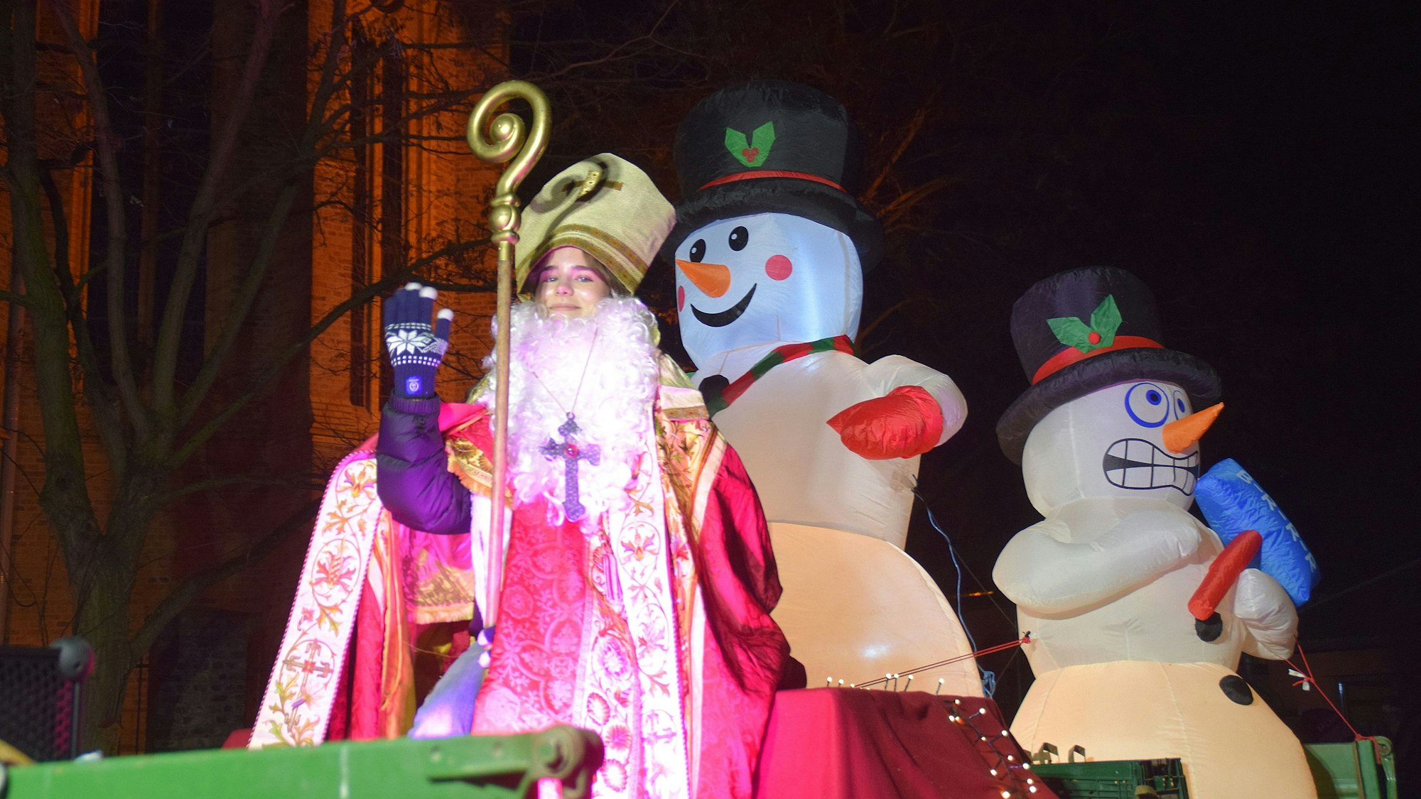 Eine Jugendliche im Nikolauskostüm sitzt auf einem Traktor und winkt. Hinter ihr sind aufgeblasene Schneemänner zu sehen.