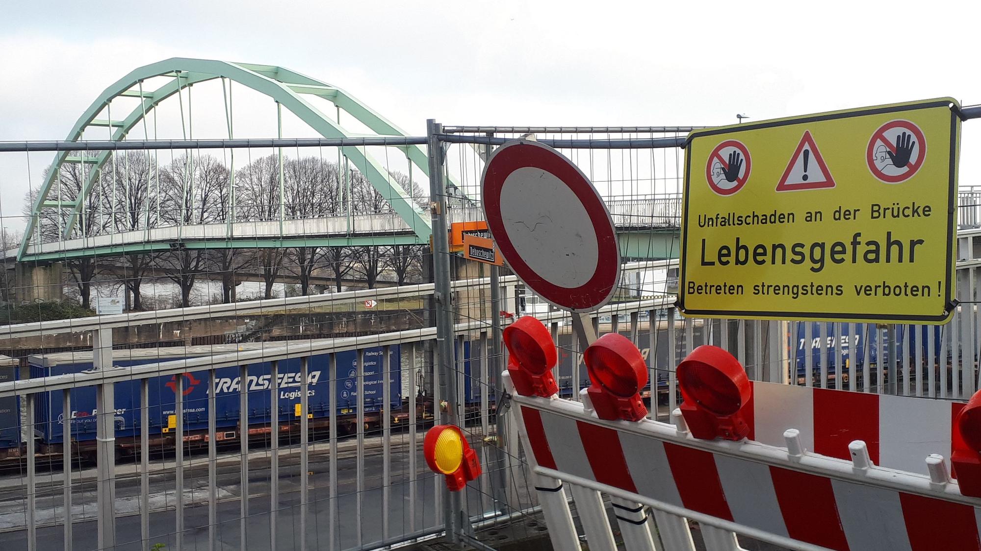 Eine Absperrung an einer Brücke mit vielen Schildern und rot-weißer Bake ist zu sehen.