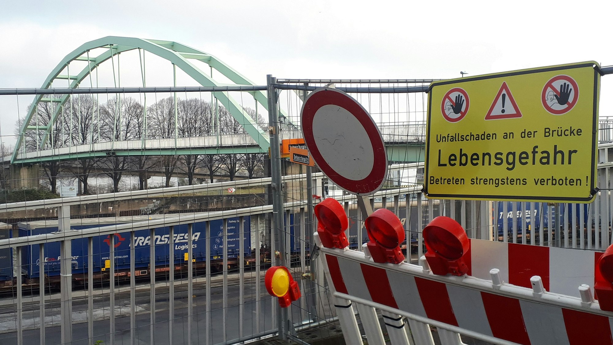 Eine Absperrung an einer Brücke mit vielen Schildern und rot-weißer Bake ist zu sehen.