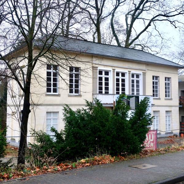 Blick auf ein Gebäude, das von Bäumen und Bauzäunen umgeben ist.