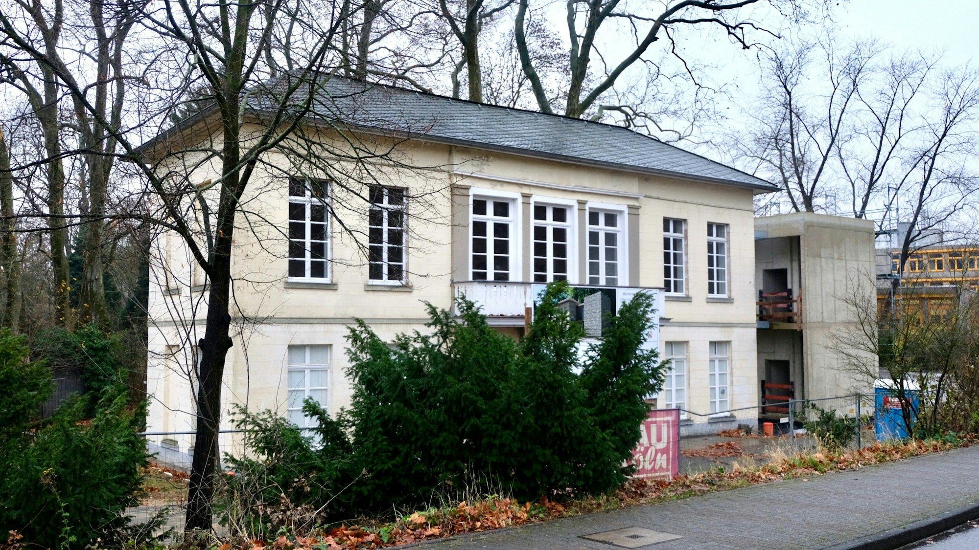 Blick auf ein Gebäude, das von Bäumen und Bauzäunen umgeben ist.