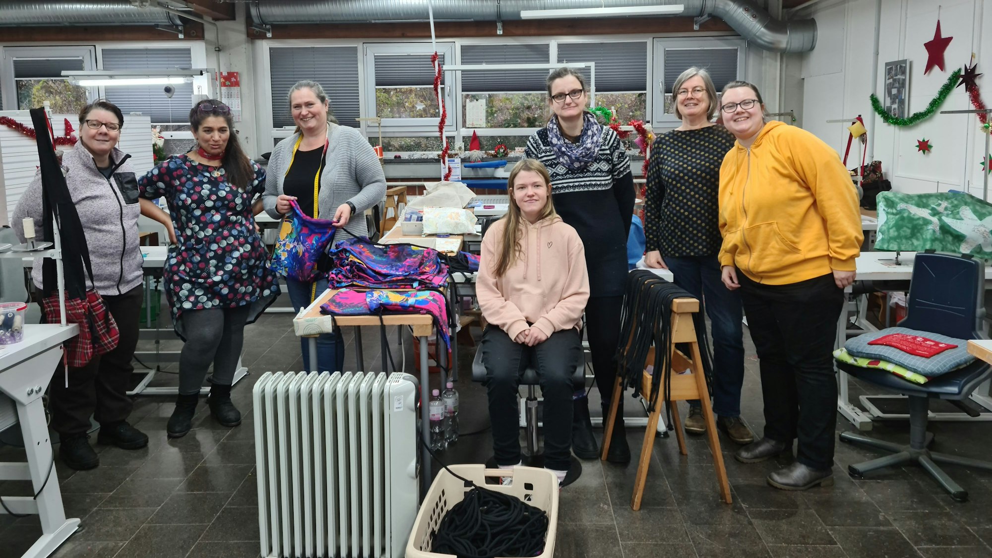 Sieben Frauen aller Altersgruppen stehen in einer Näherei.