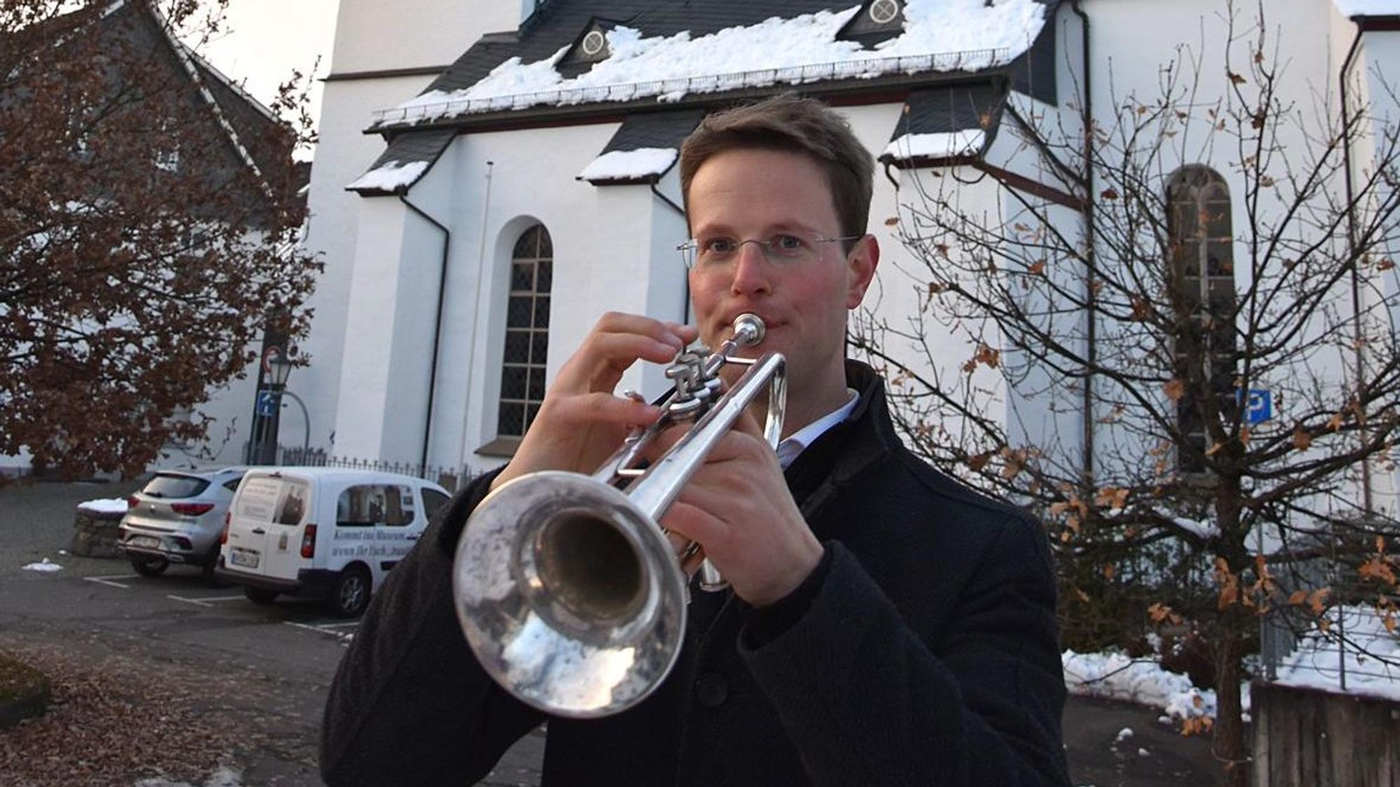 Ein Trompeter steht vor einer schneebedeckten Kirche und spielt.