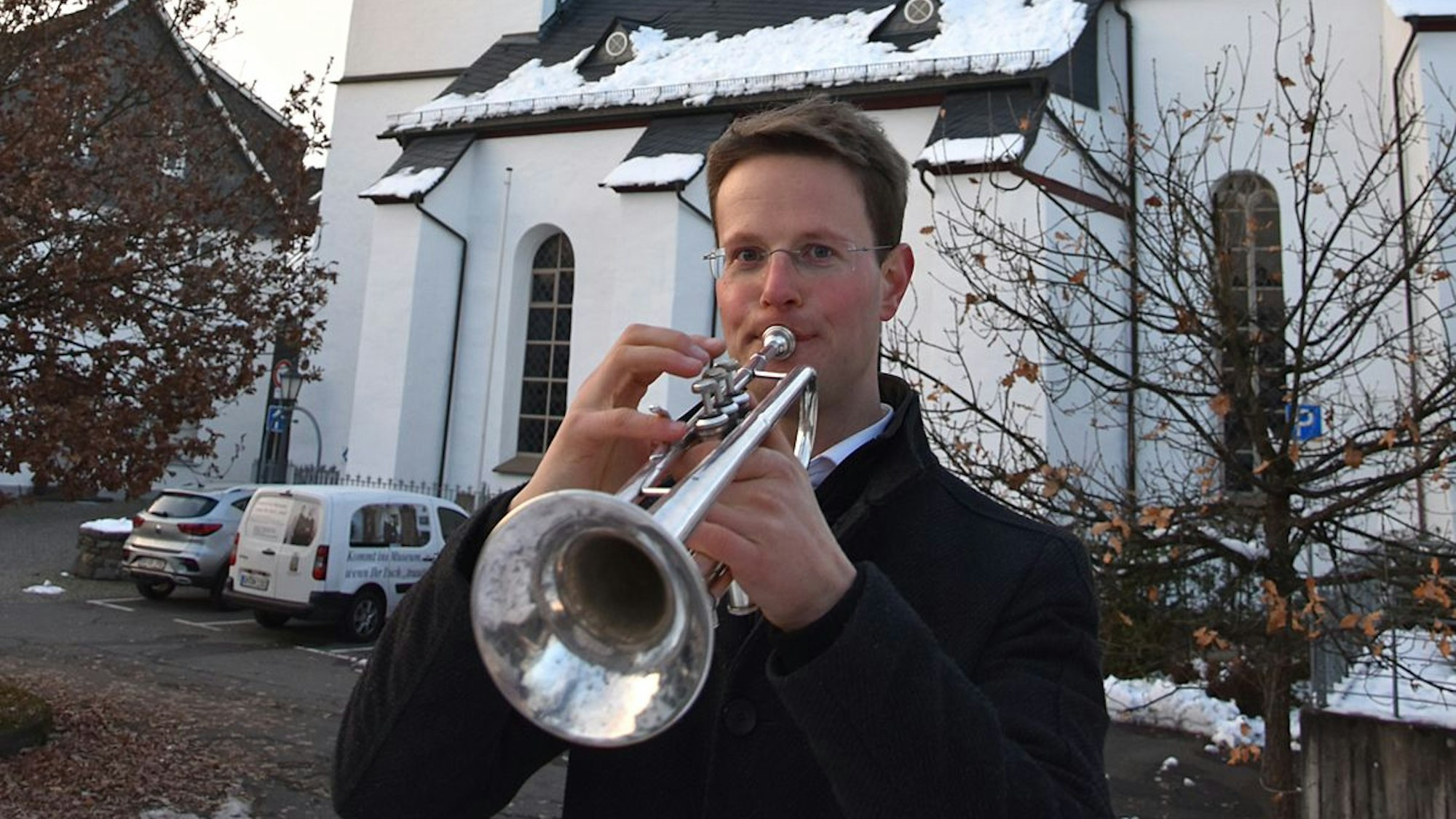Ein Trompeter steht vor einer schneebedeckten Kirche und spielt.