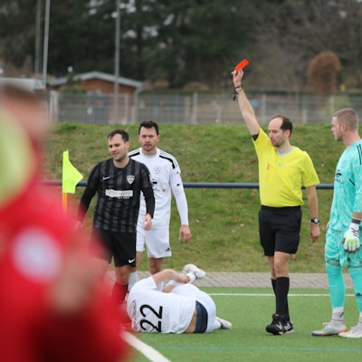Der Schiedsrichter zeigt Lein Reimer die Rote Karte. Vor ihm auf dem Boden liegt Marco Weinhold, der sich das rechte Bein festhält.