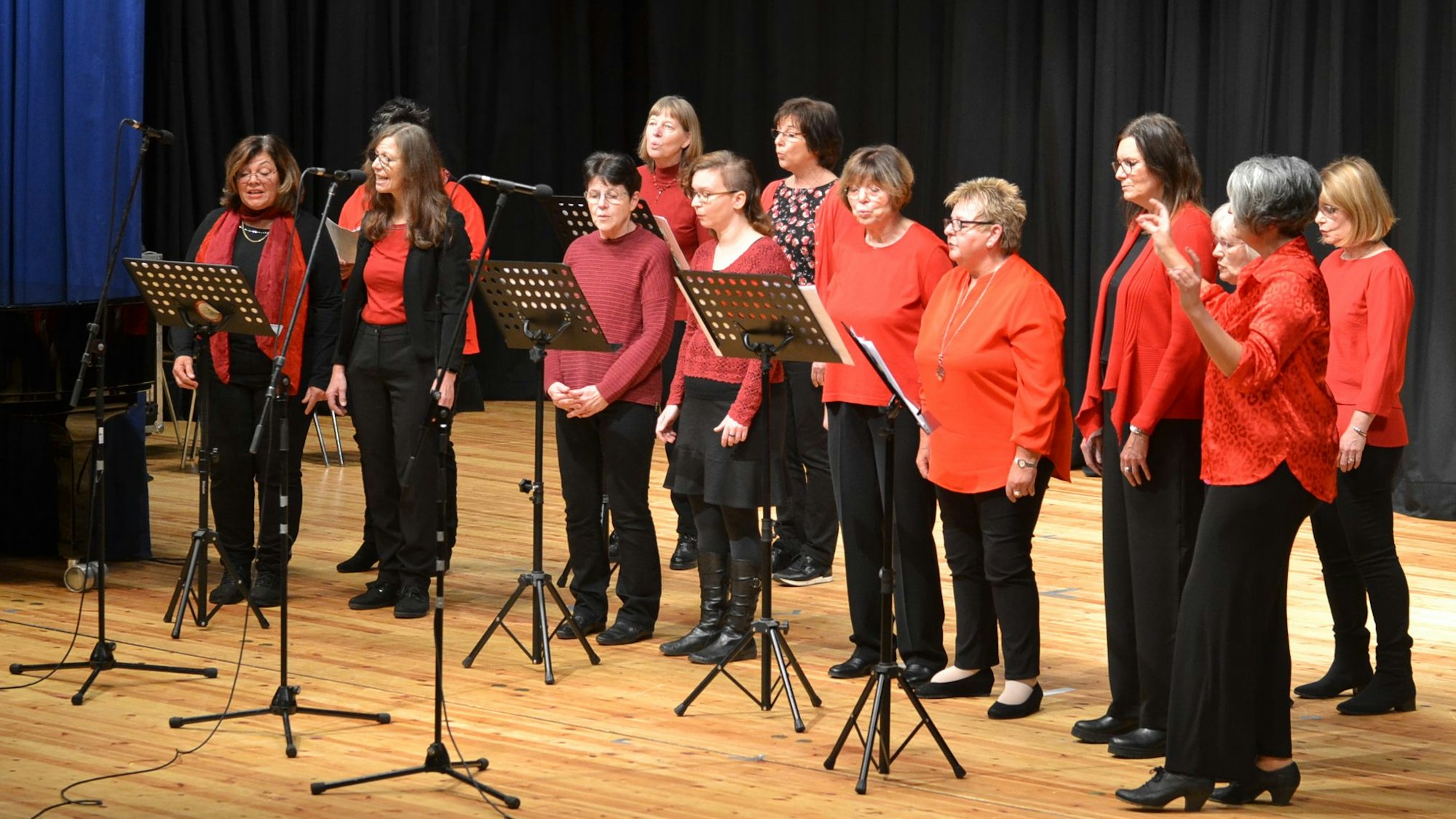 13 Frauen des Gospelchors „Go(o)d Sounds“ stehen in rot und schwarz auf einer Bühne und singen.