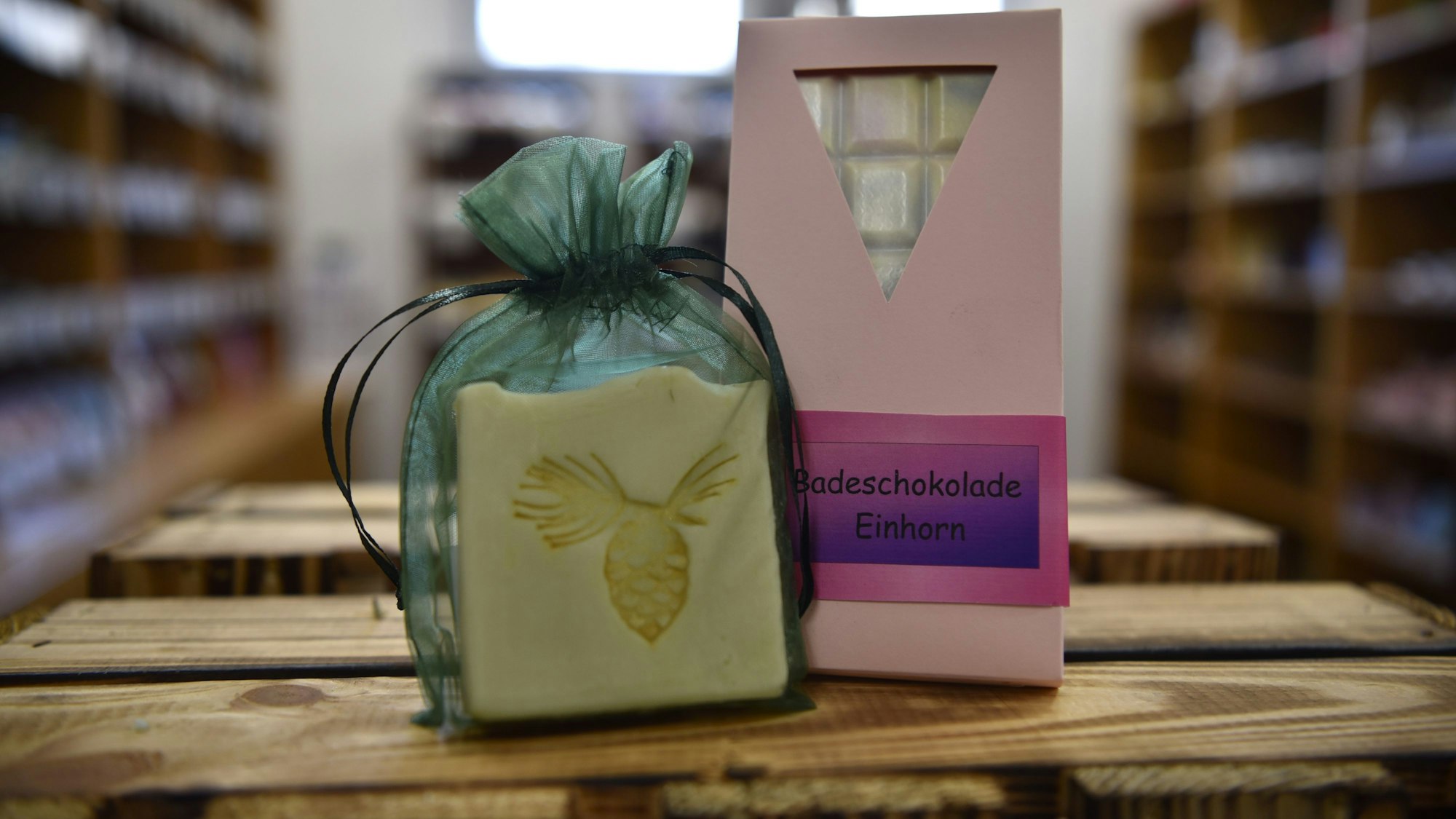 Ein verpacktes Stück Seife und eine Tafel Badeschokolade stehen auf einer Holzkiste.