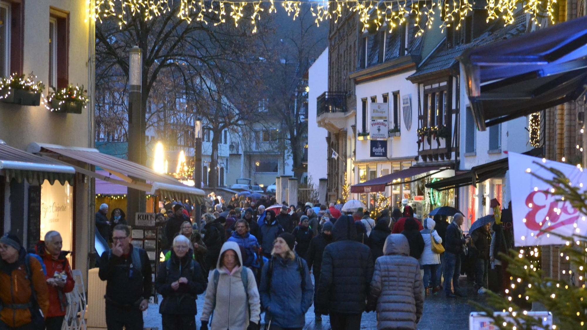 Menschen in dicken Jacken schlendern durch die weihnachtlich beleuchtete Innenstadt von Bad Münstereifel.