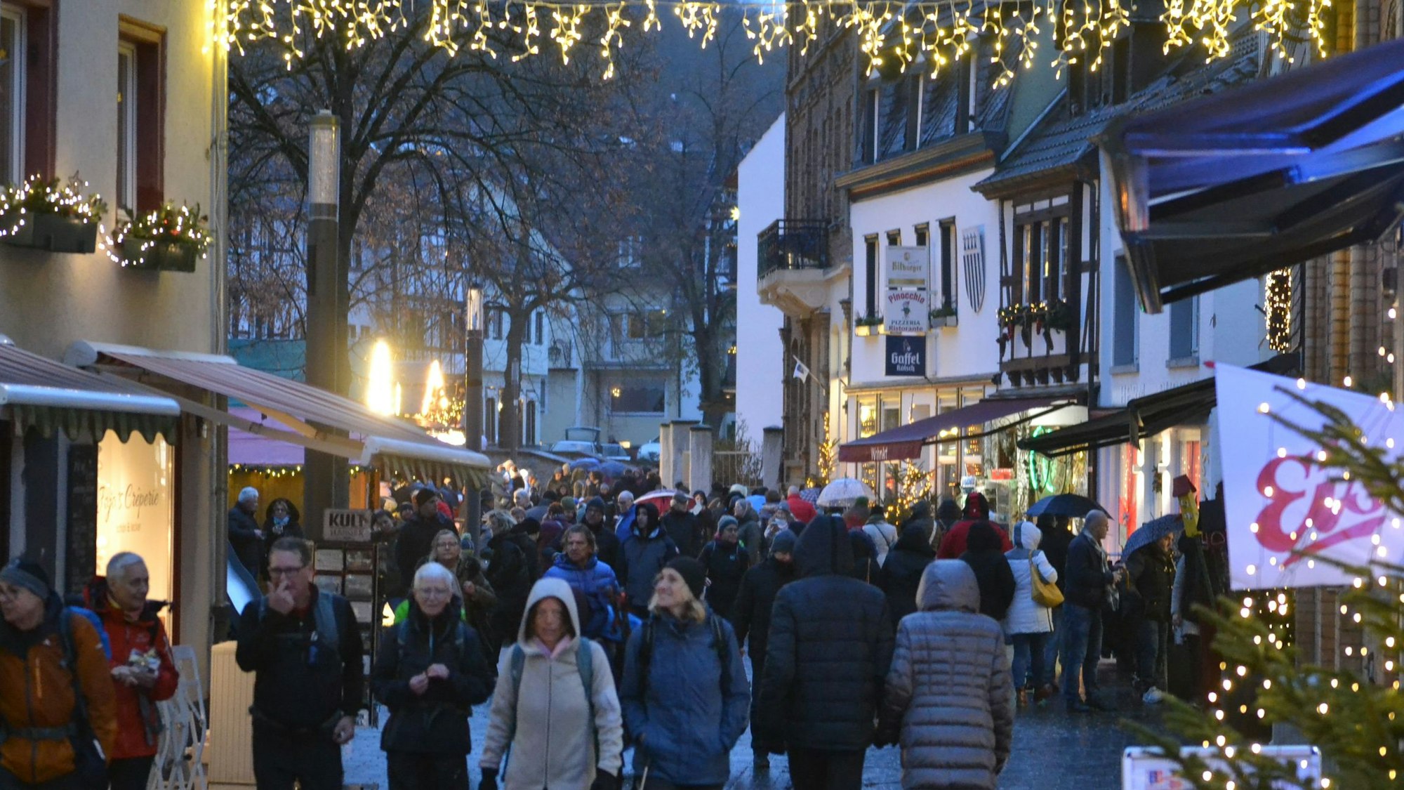 Menschen in dicken Jacken schlendern durch die weihnachtlich beleuchtete Innenstadt von Bad Münstereifel.