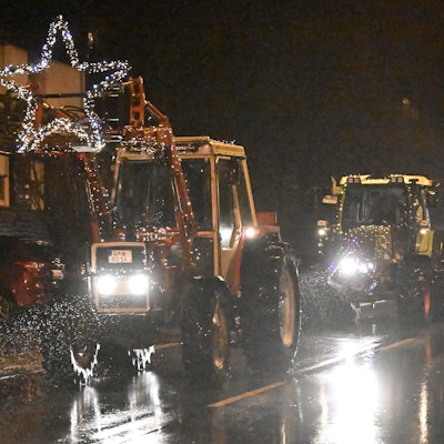 Mit Lichterketten geschmückte Traktoren fahren über eine verregnete Landstraße.