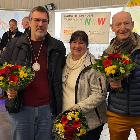 Eine Frau und zwei Männer halten Blumensträuße in den Händen.