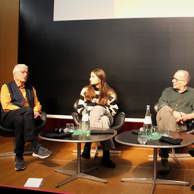 Drei Männer und eine Frau sitzen auf einem Podium.