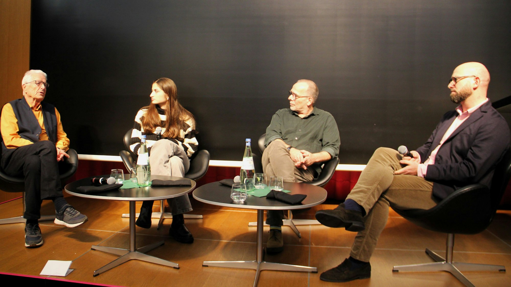 Drei Männer und eine Frau sitzen auf einem Podium.