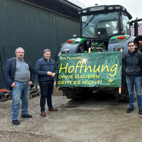 Das Foto zeigt die Landwirte und Landrat Markus Ramers neben einem Traktor, an dem ein Plakat mit der Aufschrift „Ein Funken Hoffnung. Ohne Bauern geht es nicht“ befestigt ist.