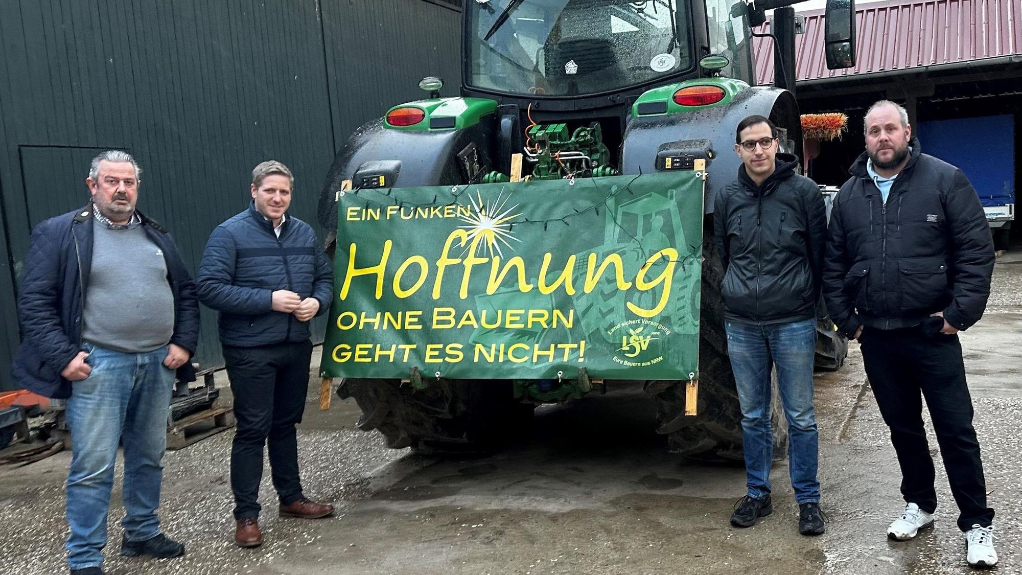 Landrat Markus Ramers und die Organisatoren stehen auf einem Hof zusammen und rahmen einen Traktor ein, der einen Banner mit der Aufschrift „Ein Funken Hoffnung. Ohne Bauern geht es nicht“ trägt.