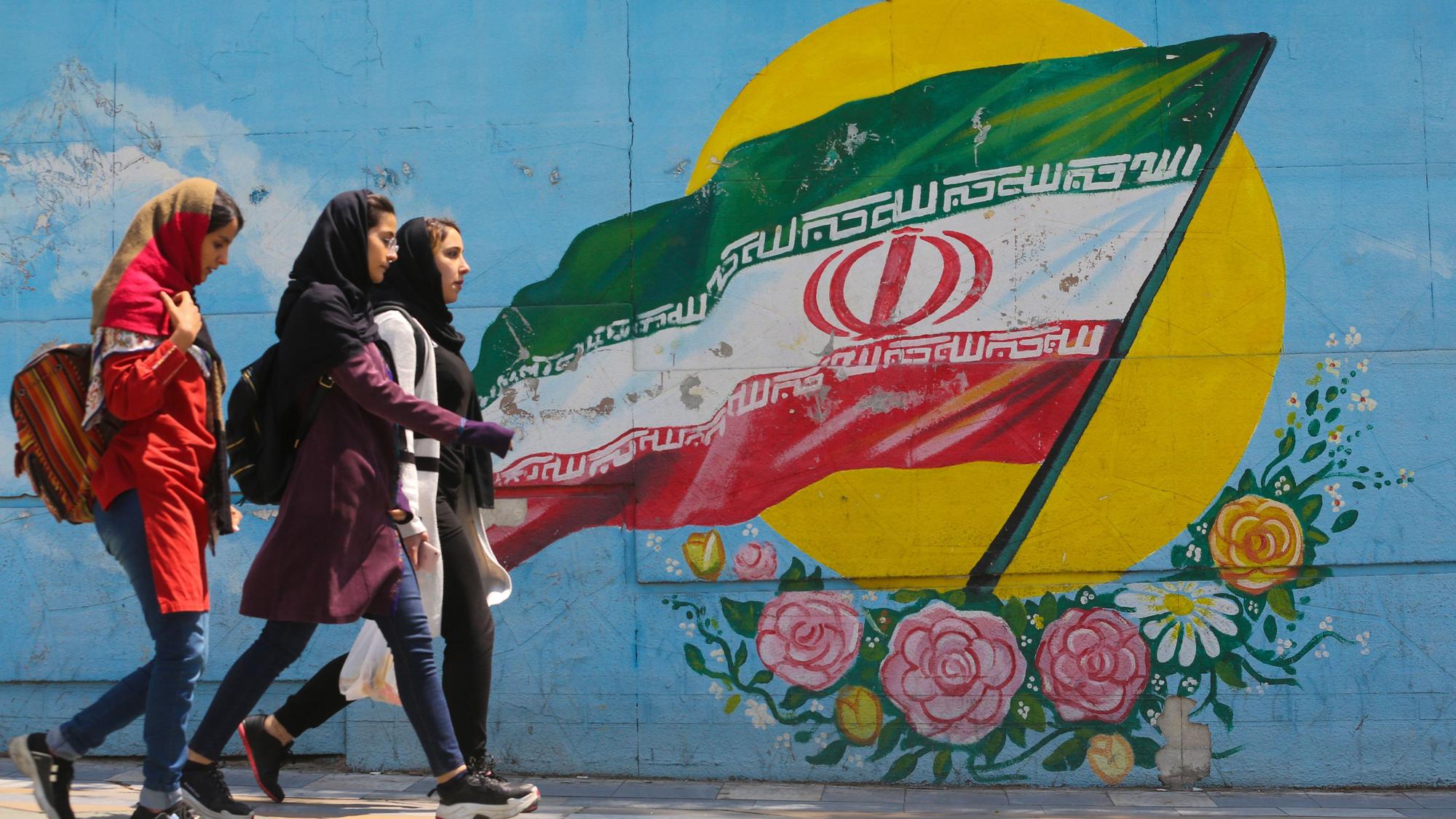Junge Mädchen laufen vor einem Wandgemälde mit der iranischen Nationalflagge im Zentrum der Hauptstadt Teheran.