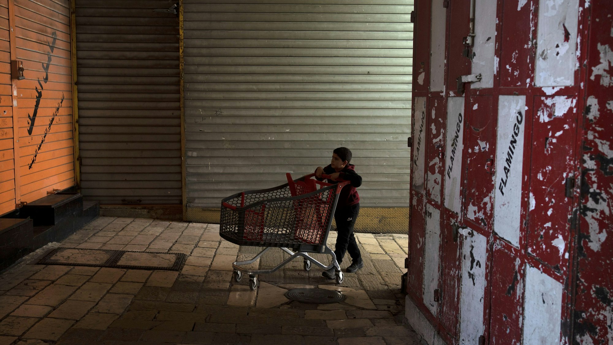 EIn Kind geht mit einem Einkaufswagen durch eine dunkle Straße.