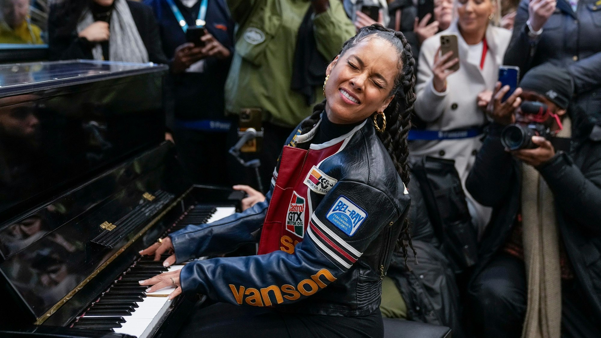 Alicia Keys sitzt an einem schwarzen Klavier. Um sie herum stehen Schaulustige.