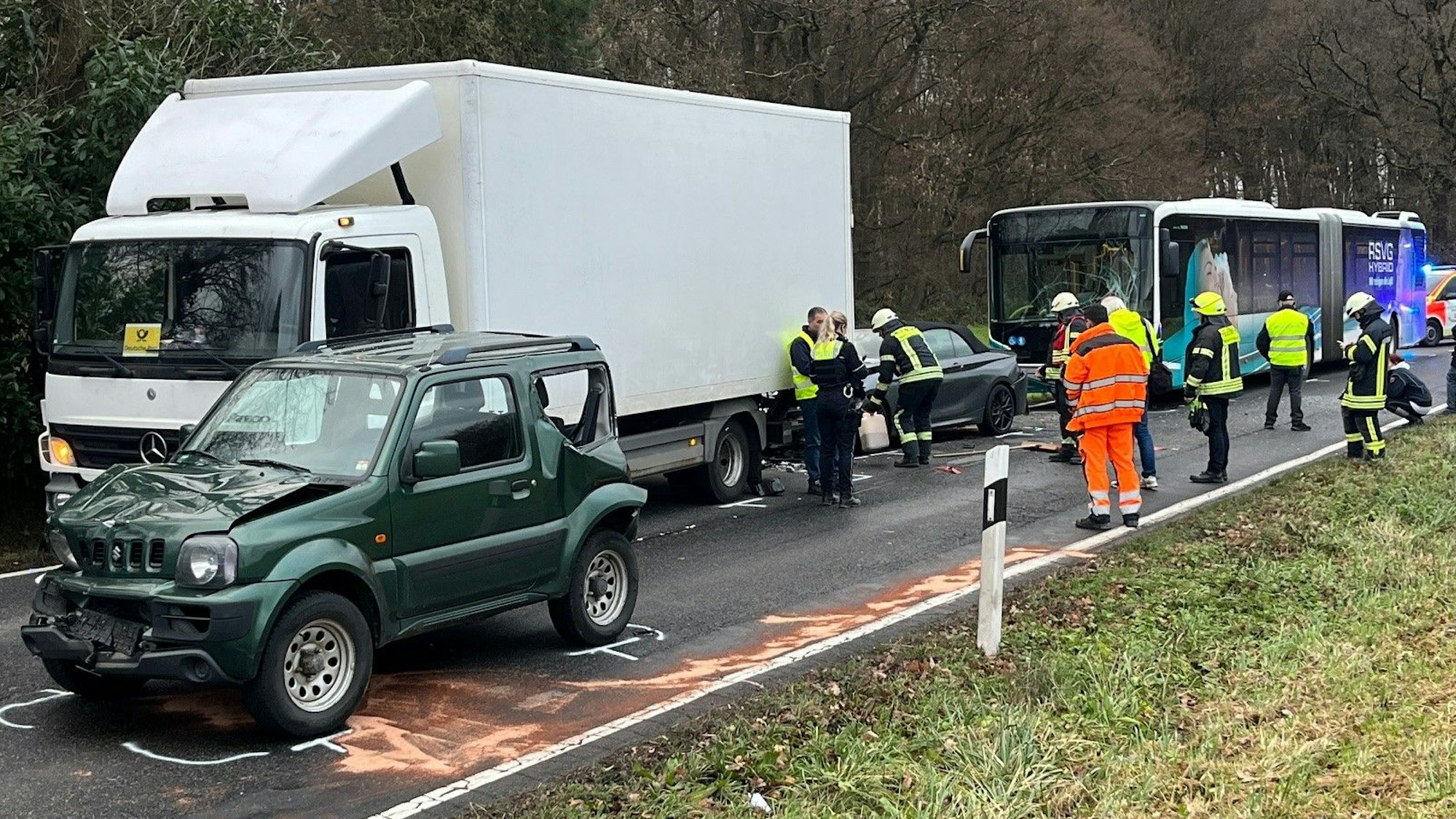 Ein Lkw, mehrere Autos und ein Bus stehen hintereinander, Feuerwehr und Rettungskräfte stehen augf der Straße.