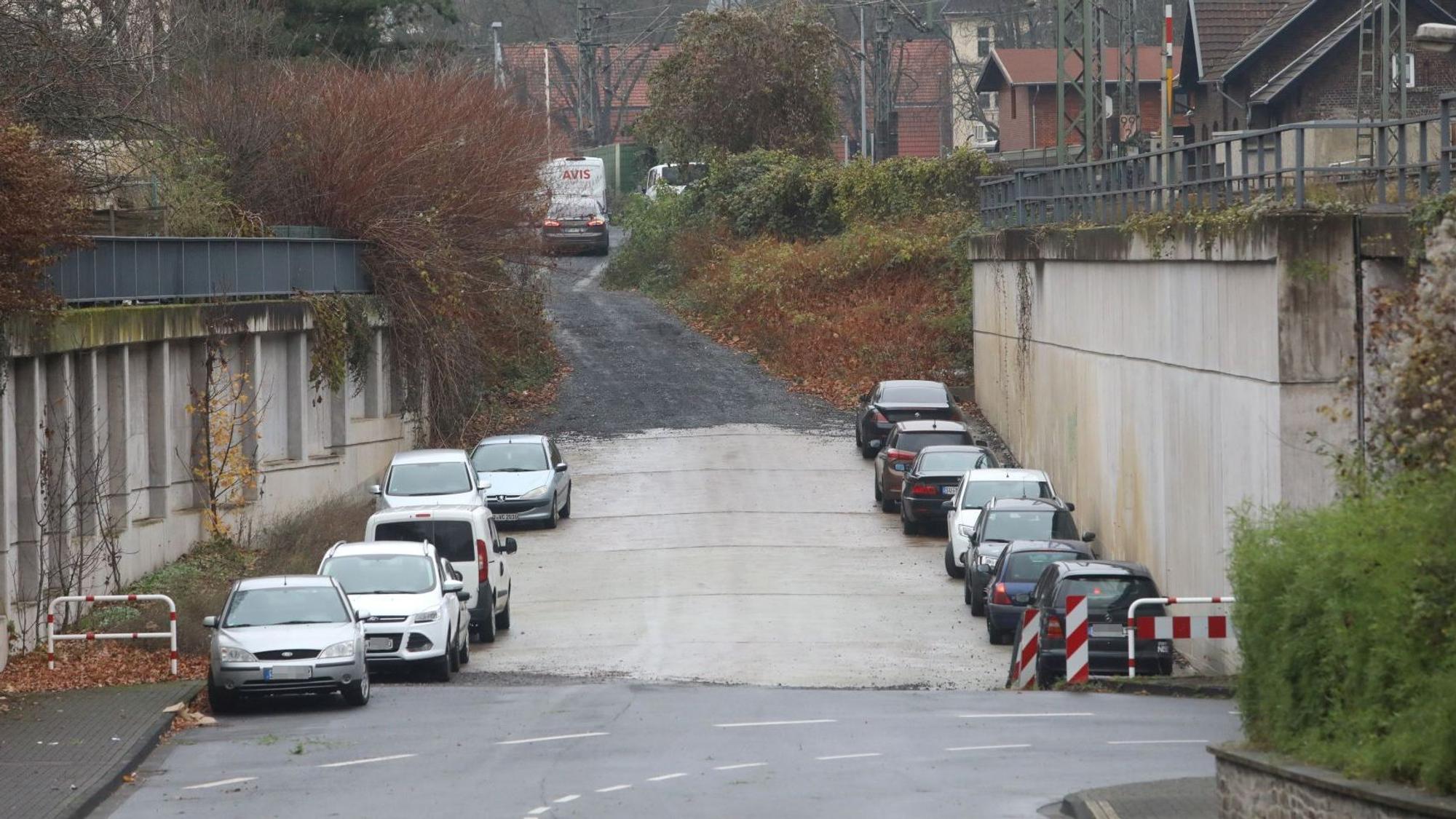Eine Fahrbahn geht auf einer Schotterstraße über, links und rechts parken Autos.