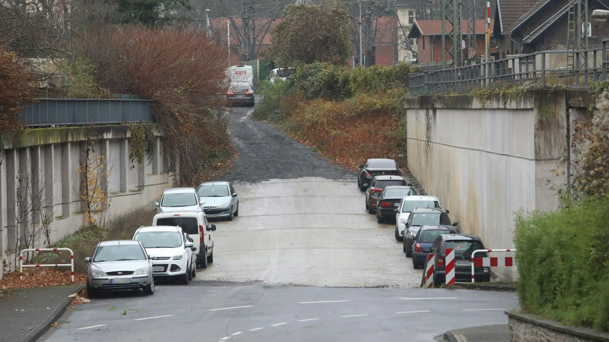 Eine Fahrbahn geht auf einer Schotterstraße über, links und rechts parken Autos.