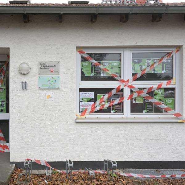 Die Eingangstür und ein Fenster des weißen Kita-Gebäudes sind mit rot-weißem Flatterband beklebt. Im Fenster hängen DinA 4 große Protestplakate.