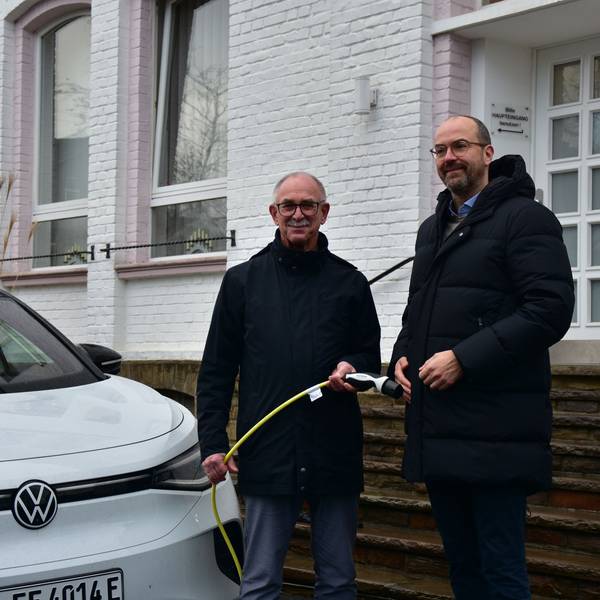Bürgermeister steht neben einem E-Auto und hält das Ladekabel in der Hand, neben ihm steht der Rhenag-Vorstand.