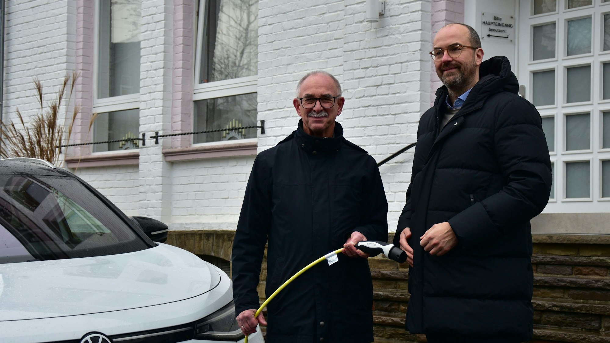 Bürgermeister steht neben einem E-Auto und hält das Ladekabel in der Hand, neben ihm steht der Rhenag-Vorstand.