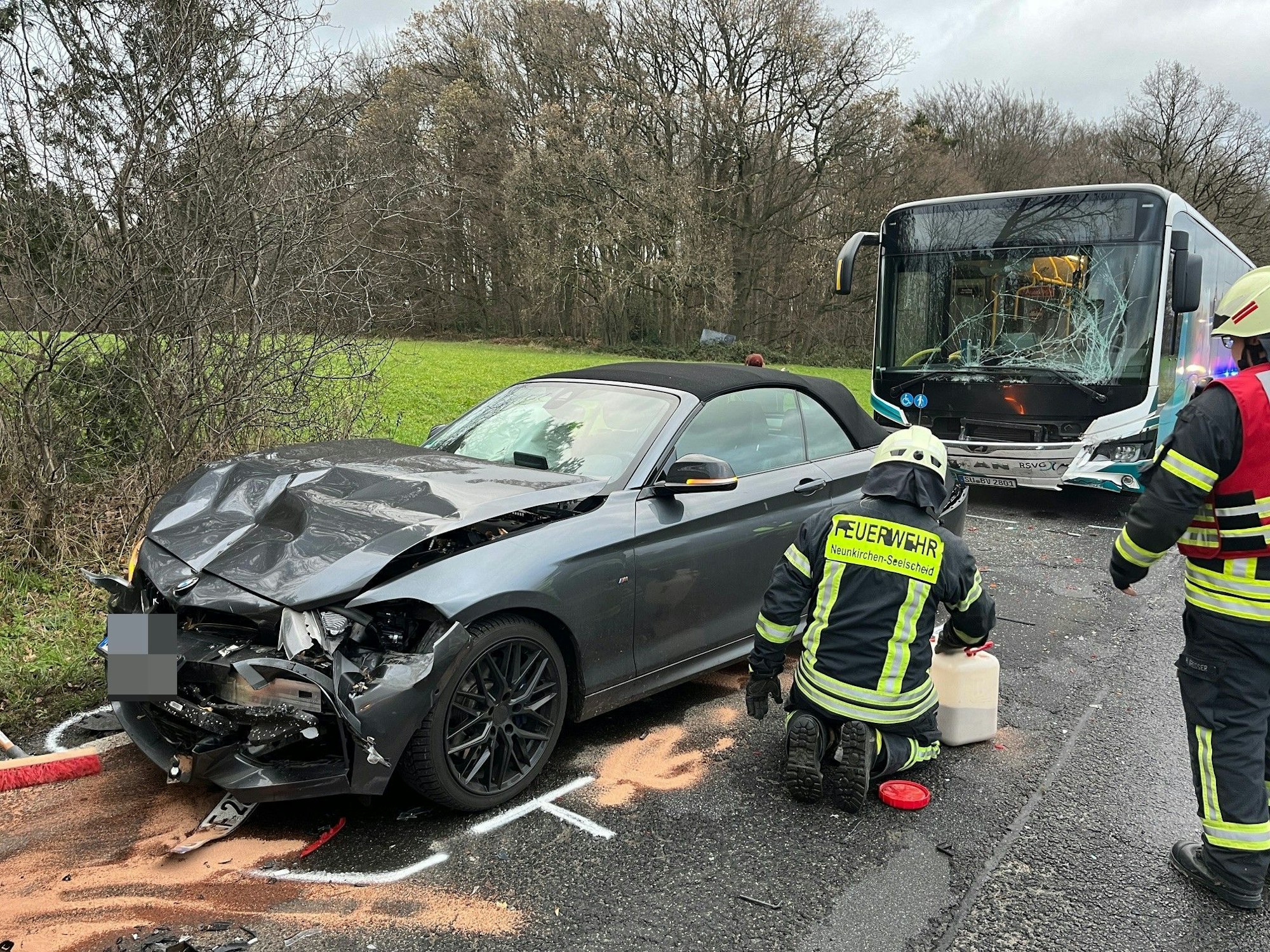 Ein schwarzer Sportwagen steht mit eingedrückter Front auf der Straße, hinter ihm ein Bus mit zersplitterter Scheibe.