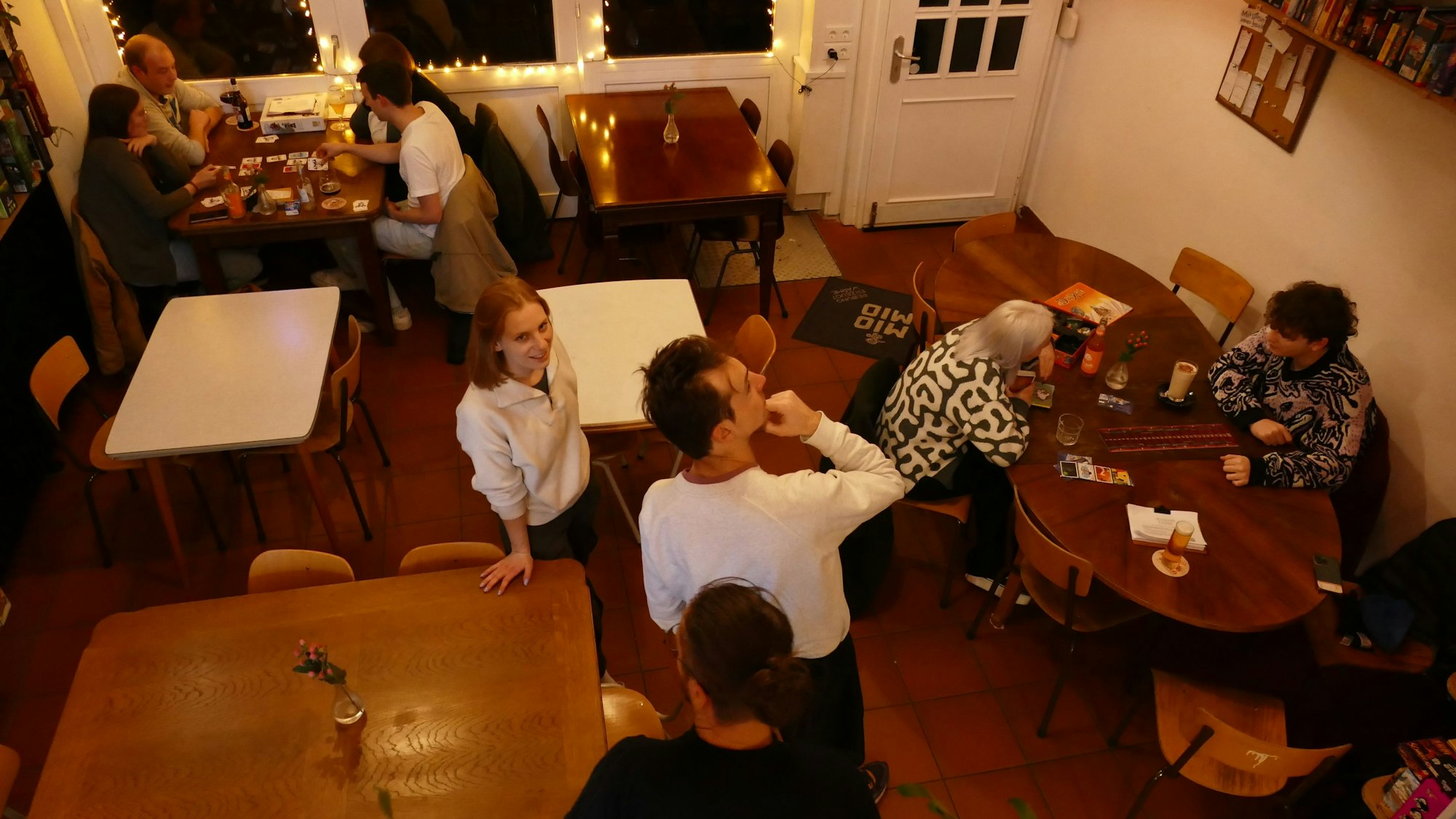 Einige Holztische sind zu sehen, an zweien sitzen Gäste und spielen.