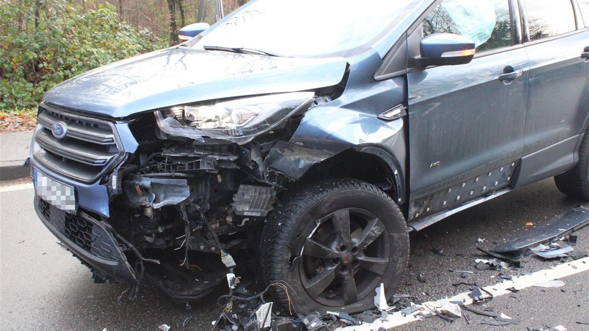 Ein Unfallwagen mit schwerem Schaden an der vorderen linken Ecke steht auf einer Straße.