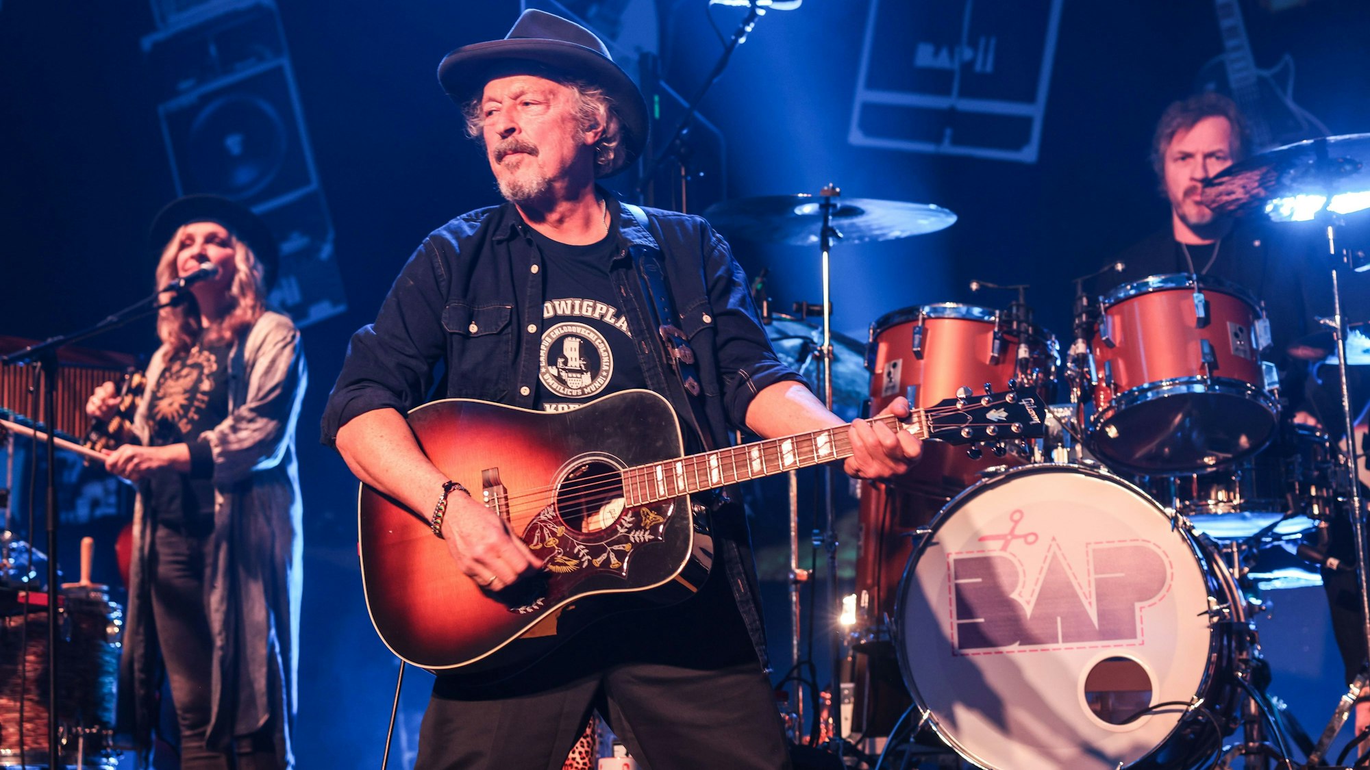 Wolfgang Niedecken (M) steht mit Anne de Wolff (l) und Sönke Reich (r) auf der Bühne.
