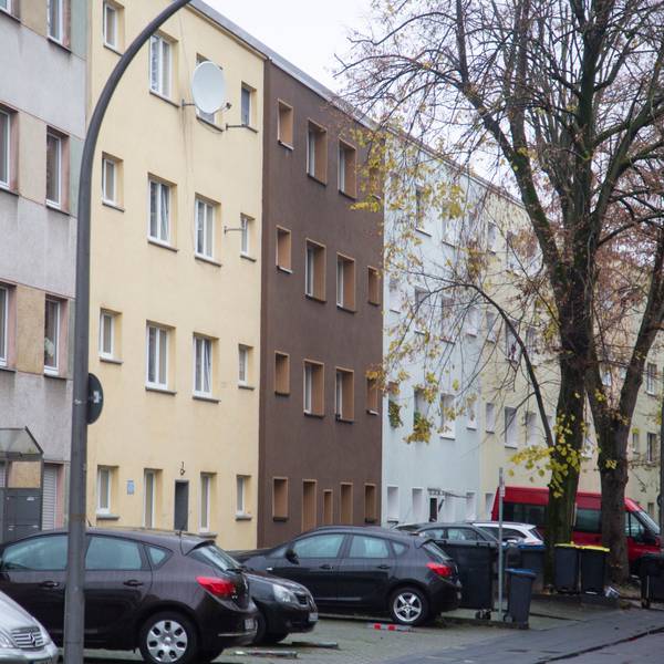 Vor einer Reihe mit Mehrfamilienhäusern sind Autos geparkt.