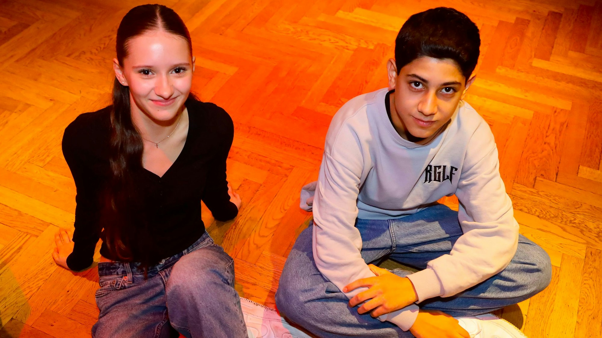 Alessia und Omid sitzen nebeneinander auf dem Boden.