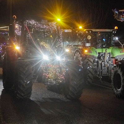 Bunt beleuchtete Traktoren fahren im Dunkeln über eine Straße.