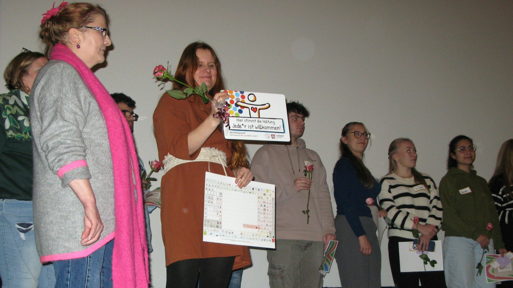 Eine Gruppe von Erwachsenen und jungen Leuten mit Rosen und Plakaten steht auf der Kinobühne.