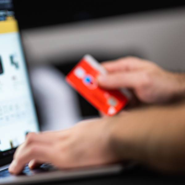 Eine Person hält eine Bankkarte in der Hand, auf einem Bildschirm sind verschiedene Kaufangebote.