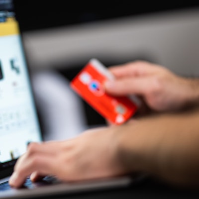 Eine Person hält eine Bankkarte in der Hand, auf einem Bildschirm sind verschiedene Kaufangebote.