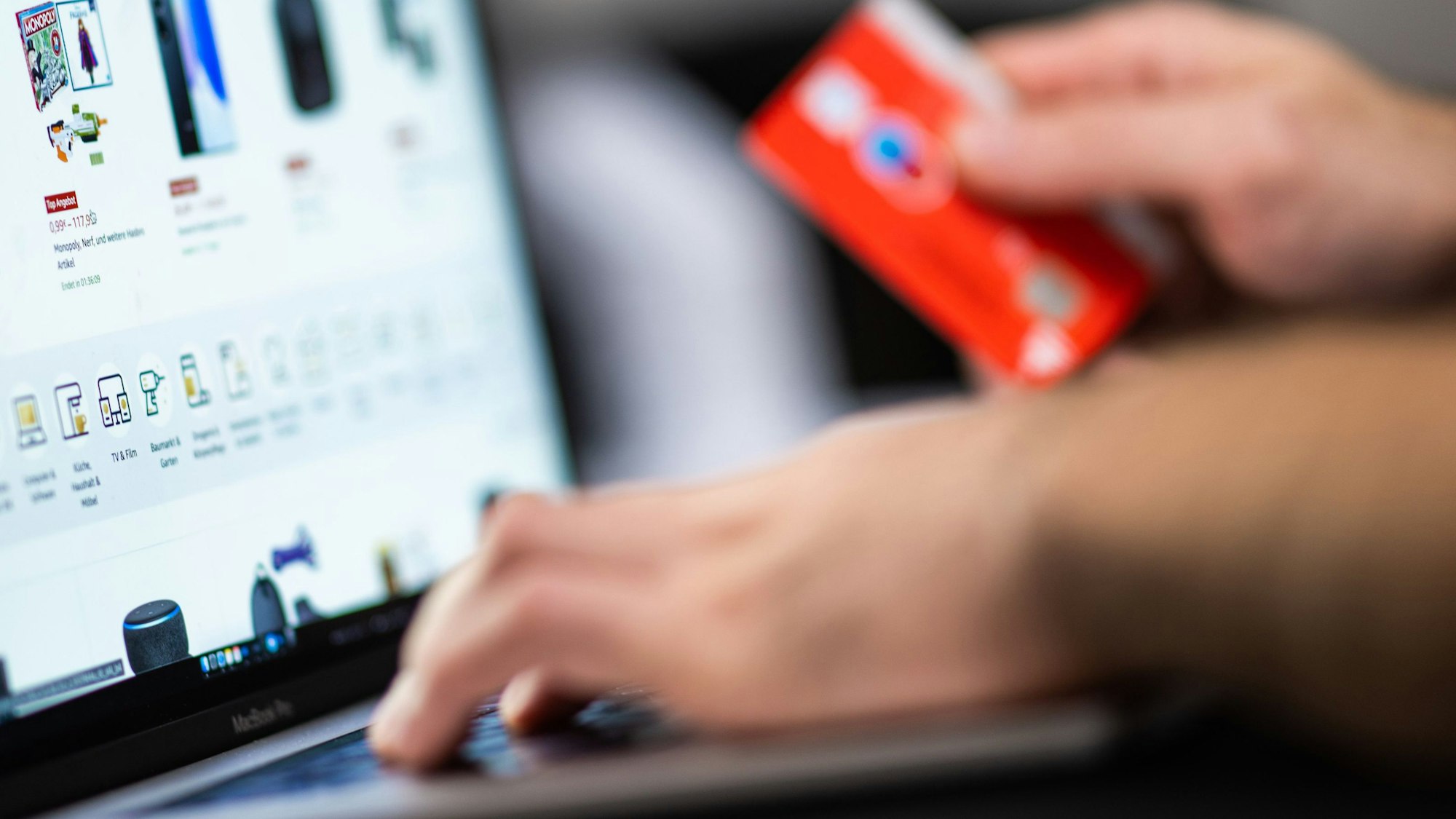 Eine Person hält eine Bankkarte in der Hand, auf einem Bildschirm sind verschiedene Kaufangebote.