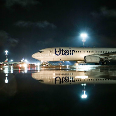 Eine Boeing 737 der russischen Fluggesellschaft UTair steht unter einem großen Scheinwerfer auf einem Rollfeld. Die Warnleuchte an den Tragflächen leuchtet. (Symbolbild)