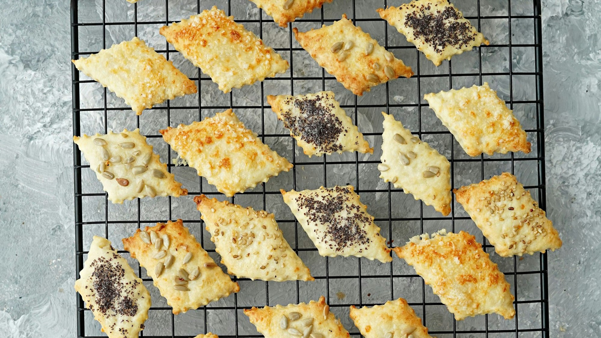 Auf einem Gitter liegen die Käseplätzchen, die unterschiedlich mit Käse, Sesam, Mohn und Sonnenblumenkernen belegt sind.