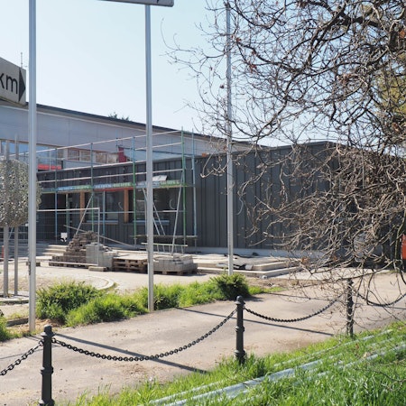 Zu sehen ist ein in die Jahre gekommenes Schulgebäude. Im vorderen Bereich entsteht ein Anbau.