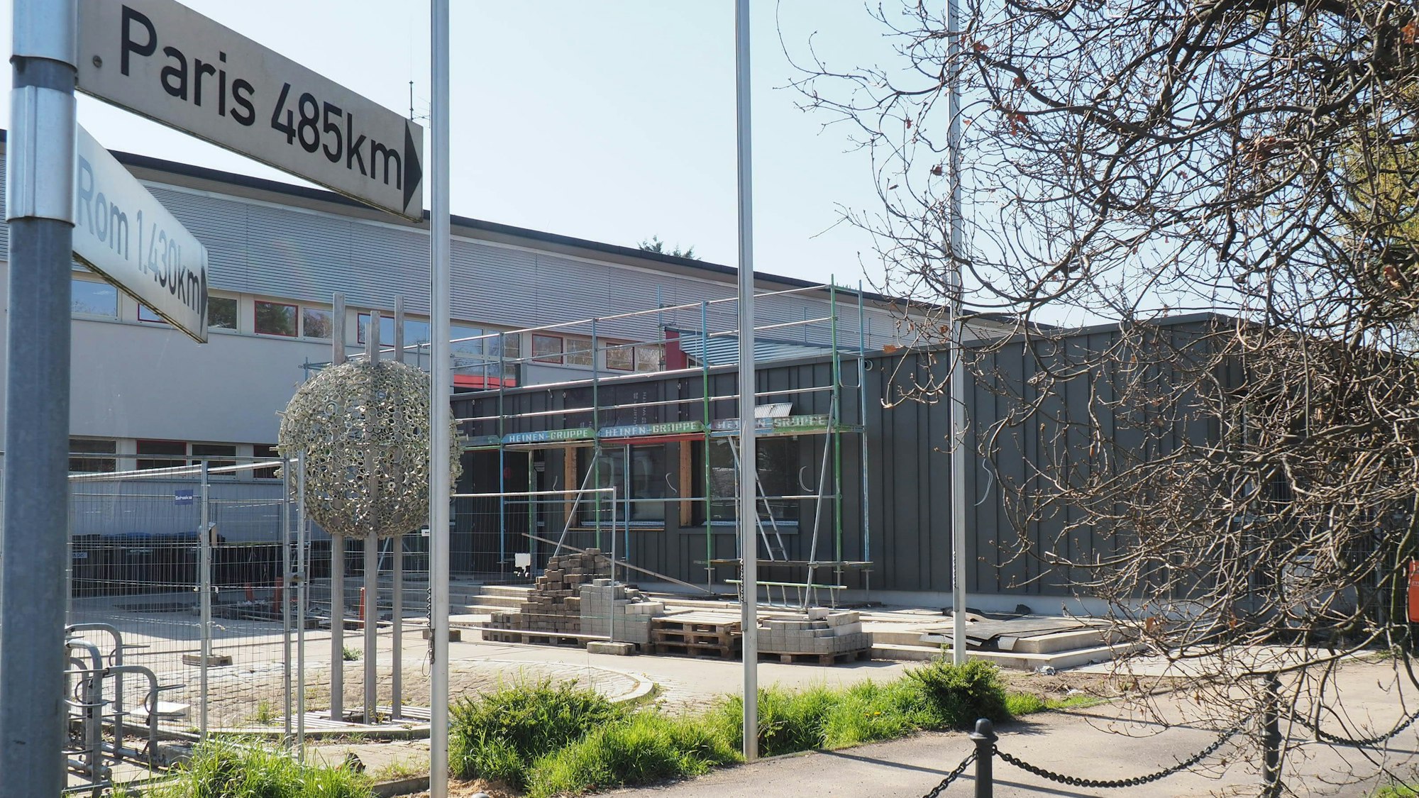 Zu sehen ist ein in die Jahre gekommenes Schulgebäude. Im vorderen Bereich entsteht ein Anbau.