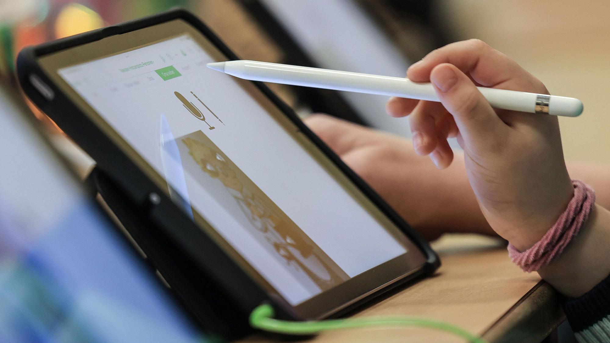 Ein Kind sitzt mit einem Stift vor einem iPad.