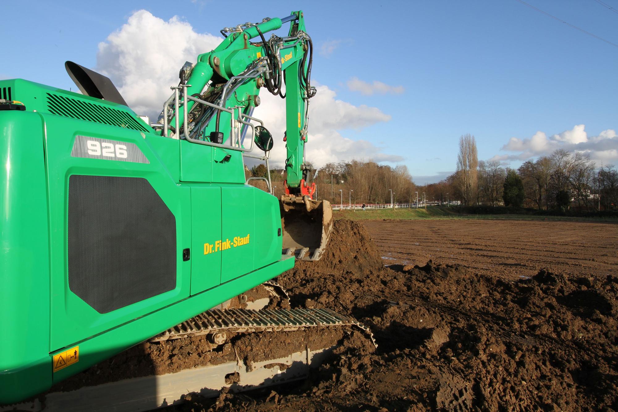 Ein grüner Bagger vor einem unbebautem Feld.