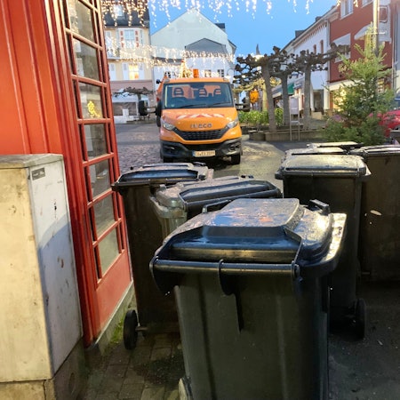 Am Rande des Alten Marktes in Euskirchen stehen graue Abfalltonnen. Im Hintergrund ein Fahrzeug der Technischen Dienste, links ein roter Bücherschrank.